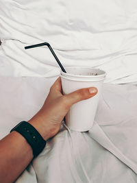 Midsection of person holding coffee cup on bed
