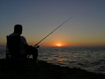 Silhouette man fishing in sea against clear sky