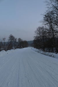 Snow covered road amidst trees against sky during winter