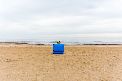 Portrait of woman behind suitcase at beach