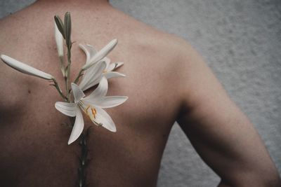 Midsection of shirtless man with flower against wall