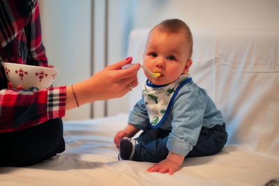 Midsection of mother feeding her baby son with spoon