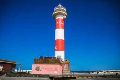 Low angle view of lighthouse by building against clear blue sky