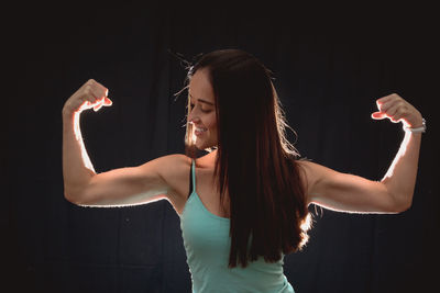 Smiling woman flexing muscles while standing against black background