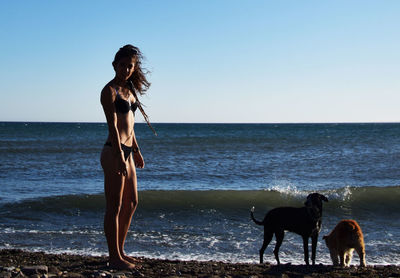 Woman with dog walking on beach against clear sky