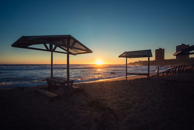 Lifeguard hut on beach against clear sky during sunset