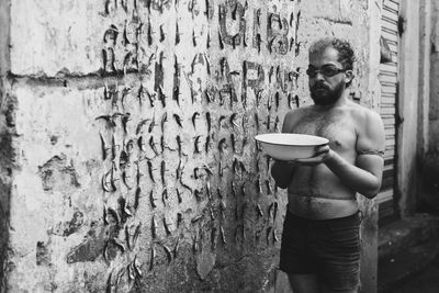 Full length of young man holding a bowl of water against wall