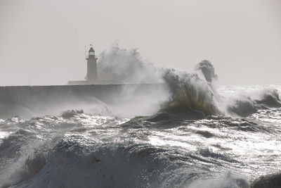 Lighthouse on sea by buildings against sky