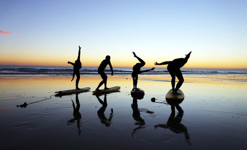 Silhouette people on beach against sky during sunset