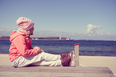 Full length of girl sitting on pier at beach