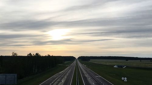 Road passing through field against cloudy sky