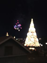 Low angle view of illuminated christmas tree against building at night