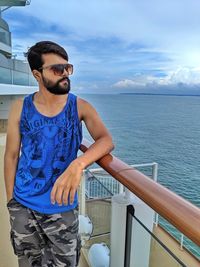 Young man wearing sunglasses standing by railing against sea