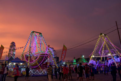 People at illuminated amusement park against sky during sunset