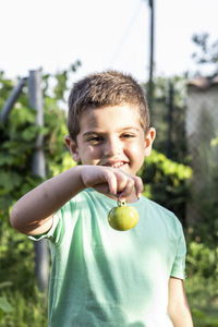 Portrait of smiling boy holding tomato on field