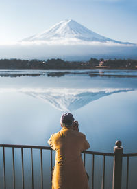 Rear view of man standing by railing on lake