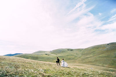 Couple holding hands walking on field against sky