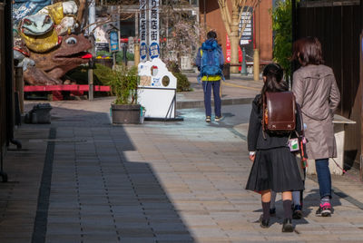 Rear view of people walking on sidewalk in city