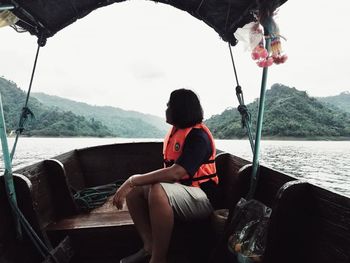 Man sitting on boat in lake against mountains