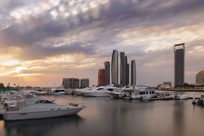 Sailboats moored on city by buildings against sky during sunset