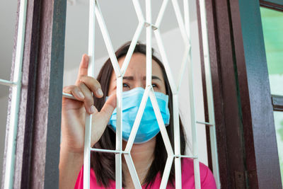 Low angel view of mature woman wearing flu mask standing by window