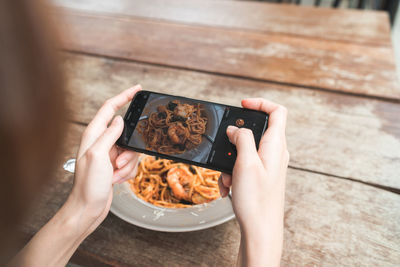 High angle view of hands photographing food with mobile phone on table