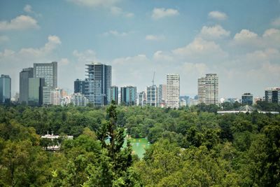 Trees and buildings in city against sky