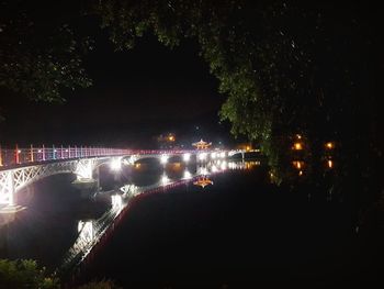 Illuminated trees by river against sky at night