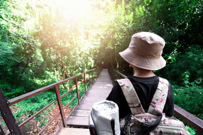 Rear view of girl wearing hat walking on wooden footbridge against trees