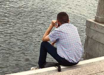 Rear view of man sitting on lake