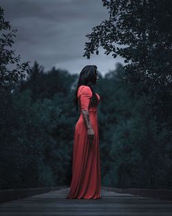 Rear view of woman standing by trees against sky