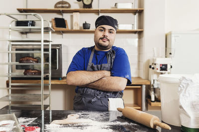 Portrait of young man standing with arms crossed in kitchen