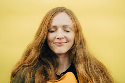 Smiling mid adult woman with eyes closed against yellow background