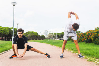 Full body hispanic male athlete lunging and bending forward with hands behind back while stretching on path during fitness workout in park