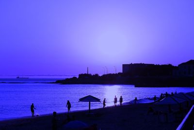 Silhouette people on beach against clear sky during sunset