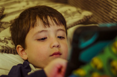 High angle view of cute boy using mobile phone while lying on bed at home