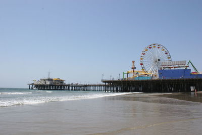 Ferris wheel by sea against clear blue sky