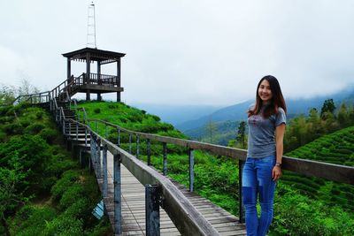 Portrait of smiling woman standing on footbridge against sky