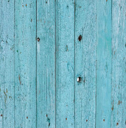 A weathered muted emerald green wood fence with loose knots and weathered cracked old paint.