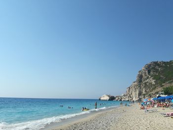 People at beach against clear blue sky