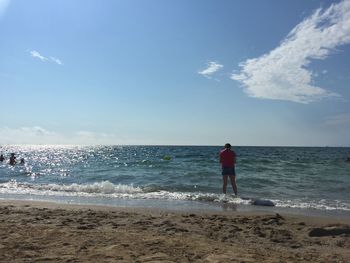 Rear view of woman standing at beach against sky during sunny day