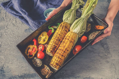 High angle view of person holding roasted vegetables in tray on table