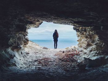 Rear view of woman standing at cave entrance