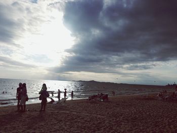 Silhouette of people on beach against cloudy sky