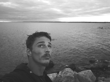 Close-up of young man standing by sea against cloudy sky