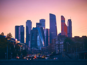 Illuminated buildings in city against sky at sunset