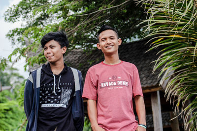 Smiling gay men standing against trees