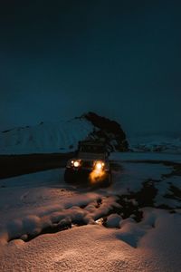 Illuminated snow covered beach against sky at night