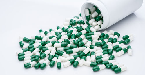 Close-up of pills spilling from bottle against white background