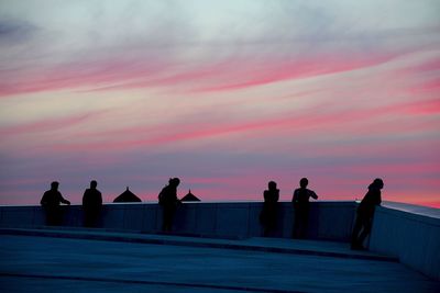 People on building terrace against sky during sunset